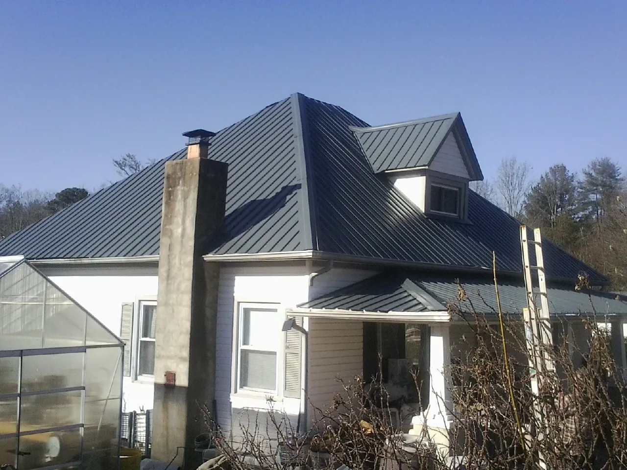 Dark blue standing seam metal roof on a white farmhouse with dormer — Slate & Tile Roof Repair by Roofing Brothers in Carmen