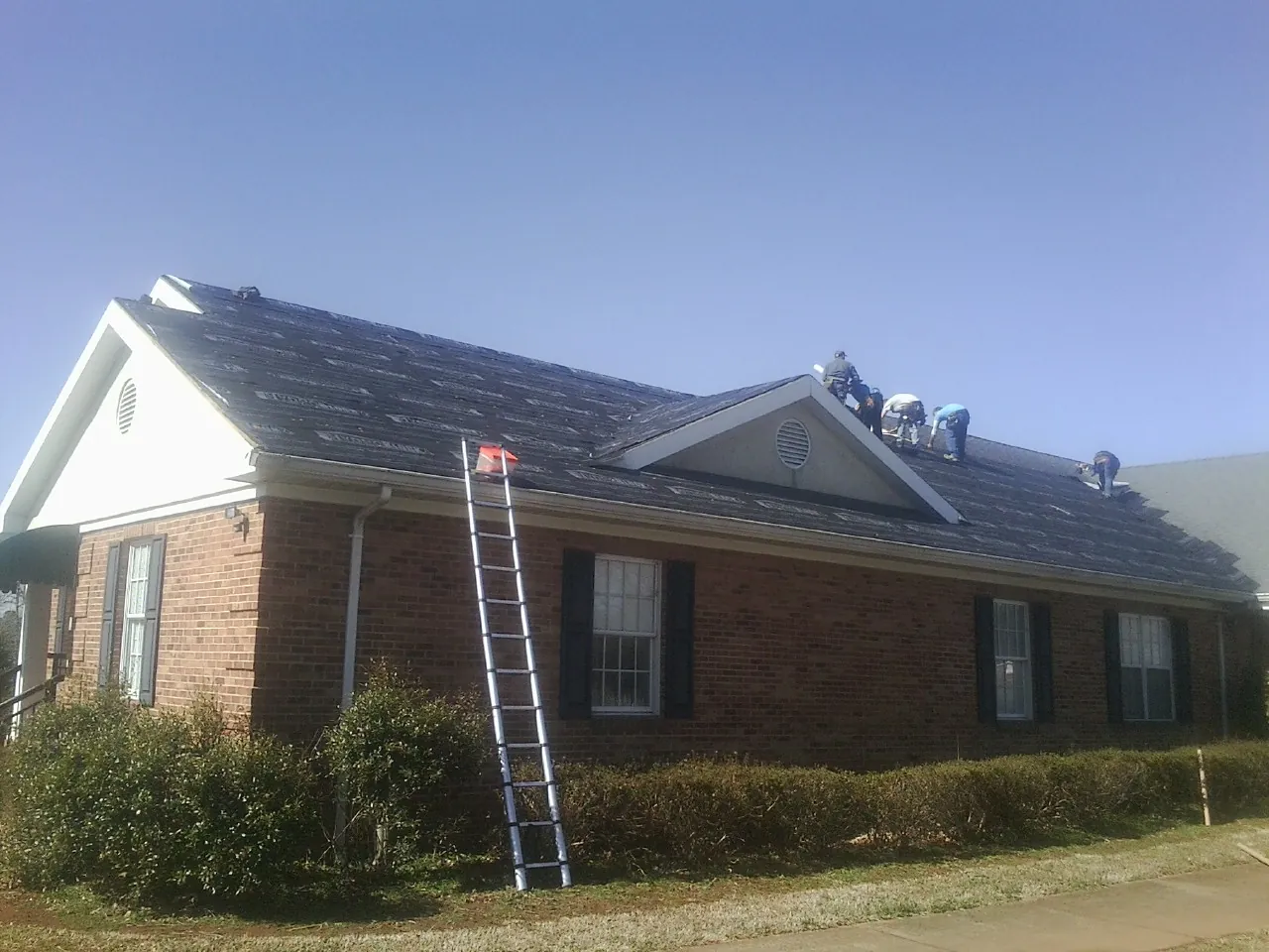 Crew tearing shingles off a brick ranch roof with a ladder set — Emergency Roof Repair work by our crew in Carmen
