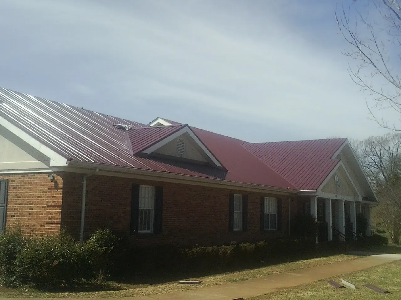 Red metal roof with gabled entries on a long brick building, from a Hail Damage Roof Repair job in Carmen