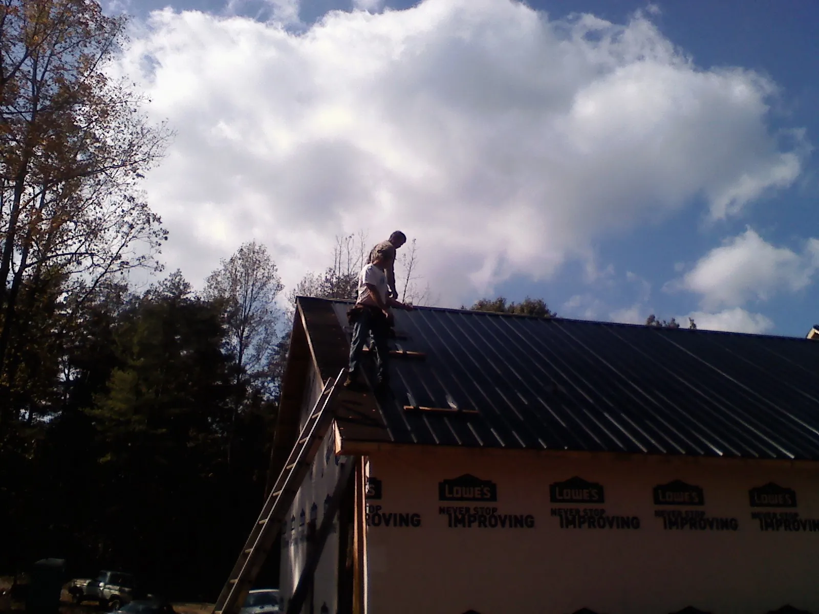 Roofer fastening dark metal panels high against a cloudy sky, from a Roof Inspection job in Carmen
